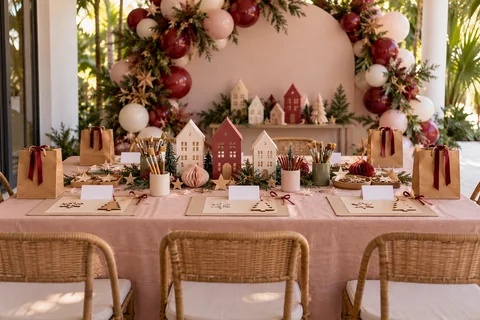A holiday craft table with paper houses, ornaments, and cranberry and blush balloon styling